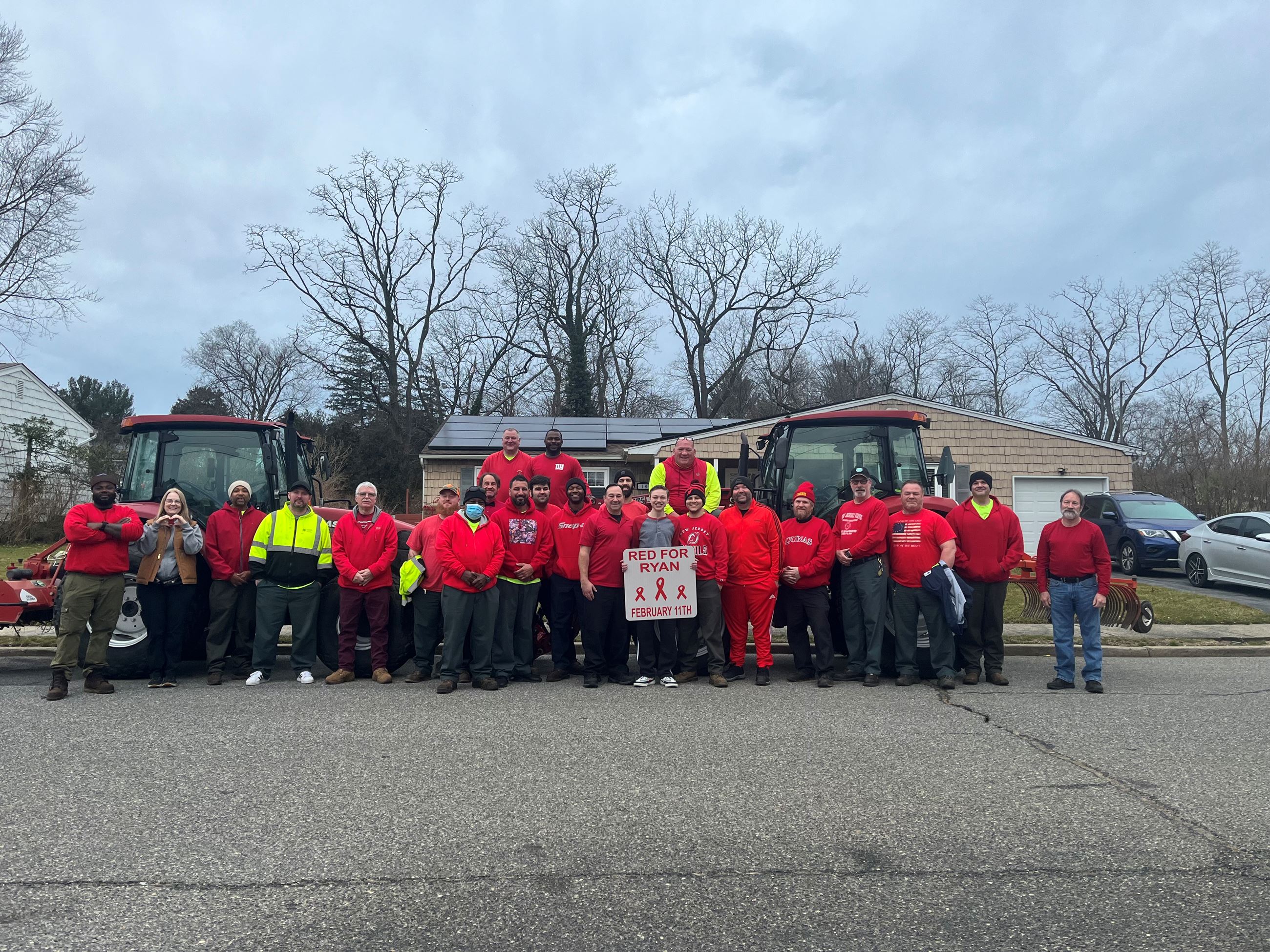 Volunteers in red and neon safety shirts pose in front of two trucks with a “RED FOR RYAN” banner dated February 11th.